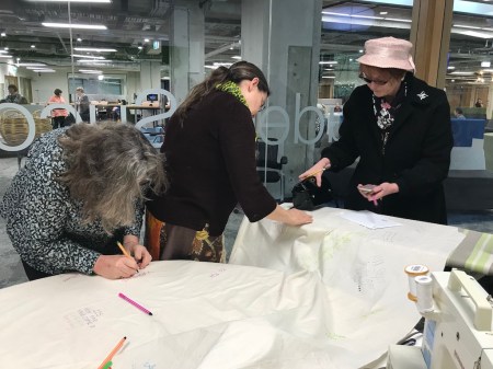 Three women siging the coat in sewing space